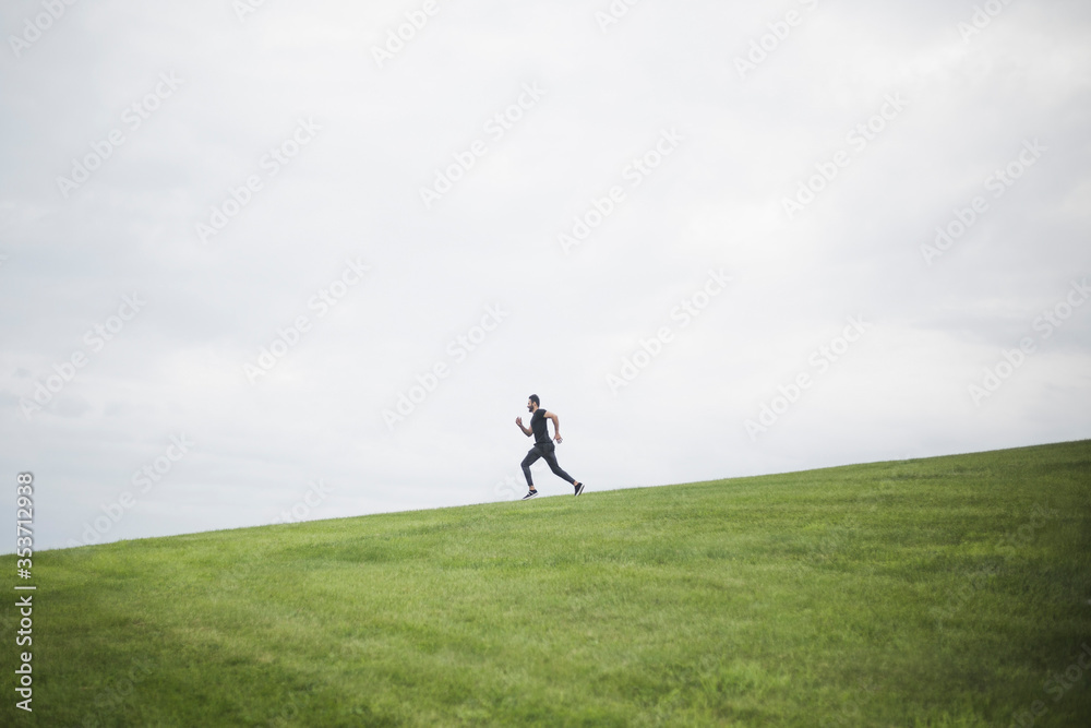 Side view of young man running on field against cloudy sky Side view of young man running on field against cloudy sky