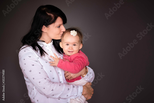 Portrait of cute baby girl and her young mother on grey background.