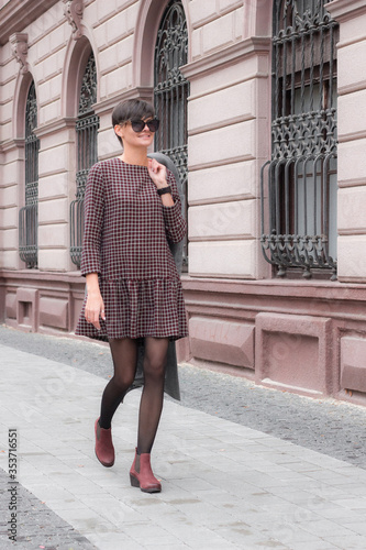 Autumn fashion outdoor. The brunette girl with short hair in fashionable stylish grey coat and sunglasses, posing on the background of building. Street fashion.Autumnal lifestyle © MONIUK ANDRII