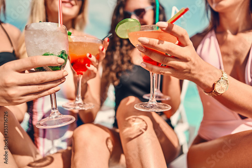 Obraz na plátně Women clinking glasses with cocktails at poolside