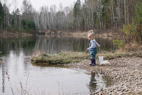 Little girl in rubber boots catches and feeds fish on the river in a jar © olgalisa88