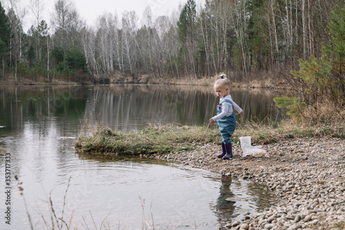 Little girl in rubber boots catches and feeds fish on the river in a jar