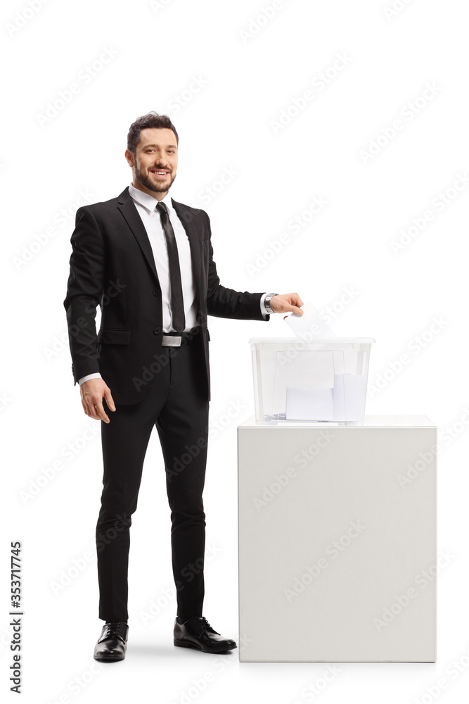 Man in a suit casting a vote in a ballot box and looking at the camera Man in a suit casting a vote in a ballot box and looking at the camera