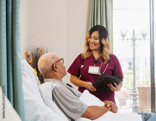 Smiling nurse holding clipboard by senior man in bed photo