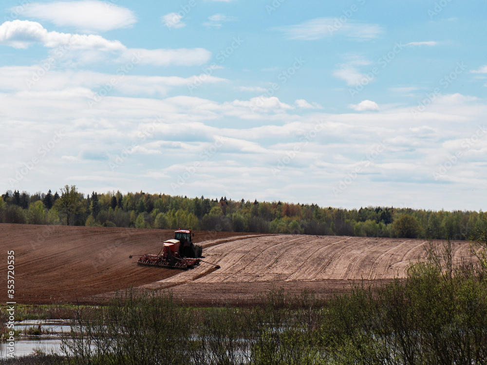 Fototapeta premium the tractor is sowing corn on the field. agriculture, farming. near the forest and the river