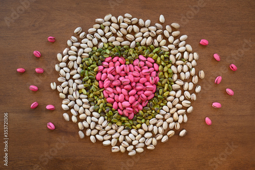Bright red-dyed and natural pistachios form a heart on warm brown wood.