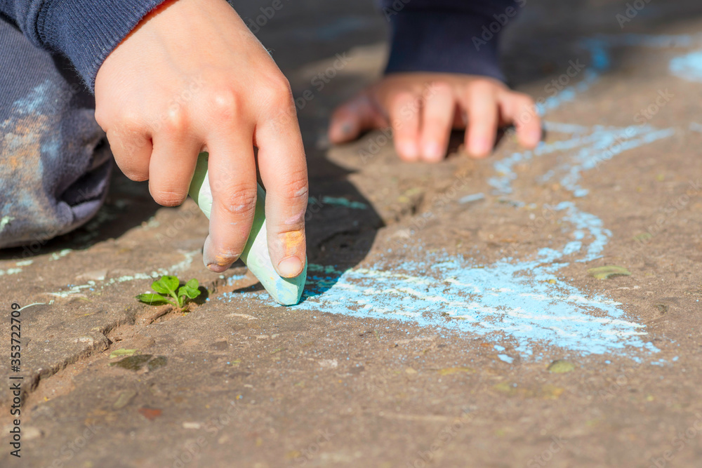 The child drawing a chalk on asphalt. Child drawings paintings on asphalt concept. Kid is playing with colored chalks The child drawing a chalk on asphalt. Child drawings paintings on asphalt concept. Kid is playing with colored chalks