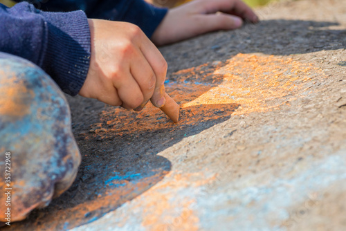 The child drawing a chalk on asphalt. Child drawings paintings on asphalt concept. Kid is playing with colored chalks