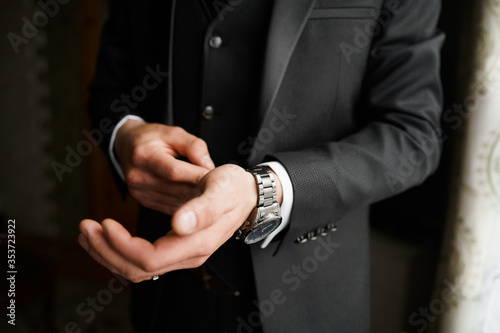 Grooms morning preparation, handsome groom getting dressed and preparing for the wedding, wearing cufflinks. Stylish groomsmen. Businessman. Luxury man in suit in room. Wedding day. Marriage.