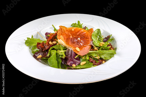 Gourmet Goat cheese salad with arugula, dried tomatoes, and nuts on a plate, isolated on black background