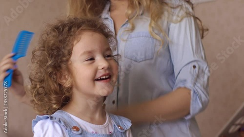 blonde curly hair mother and daughter together at home in bedroom brushing hair and smile