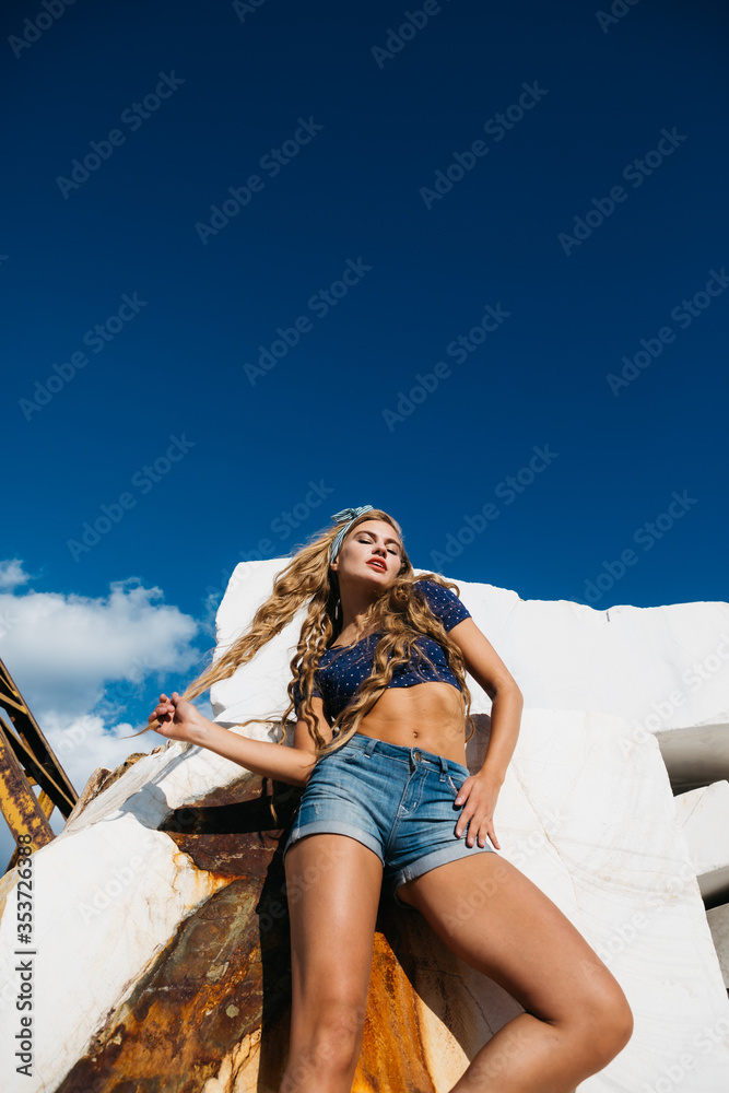 Pin-up girl with long hair posing on a large marble rock