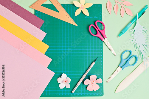 Top view over paper cut tools, scissors, cutter, cutting mat, and crafted paper objects. DIY trendy project concept