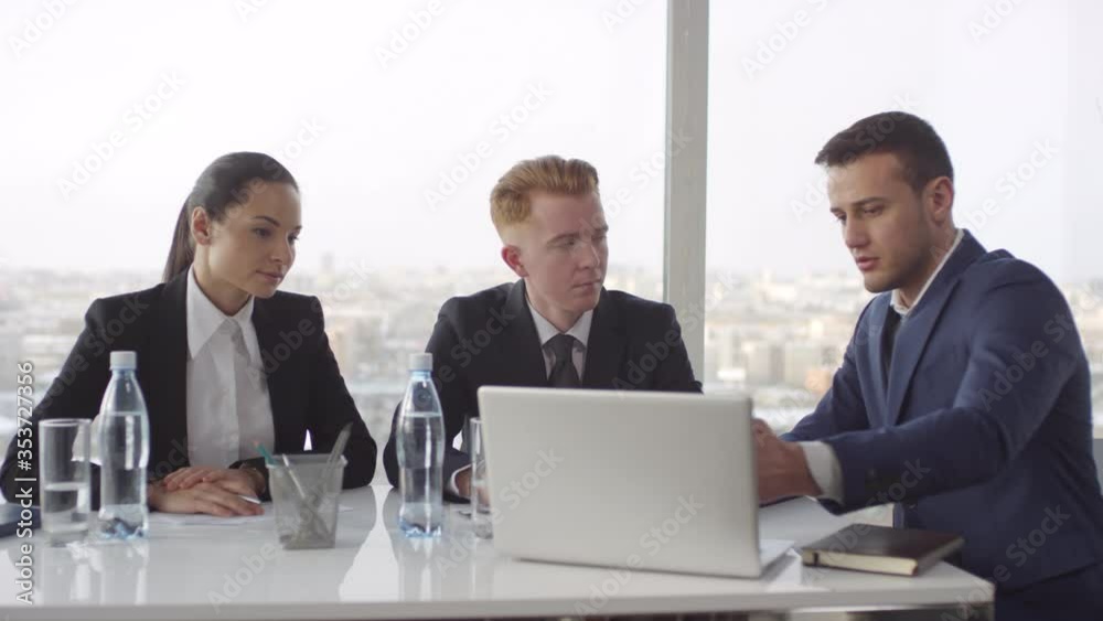 Tracking of male executive in suit sitting at table in meeting room with panoramic window and discussing work with businesspeople Tracking of male executive in suit sitting at table in meeting room with panoramic window and discussing work with businesspeople