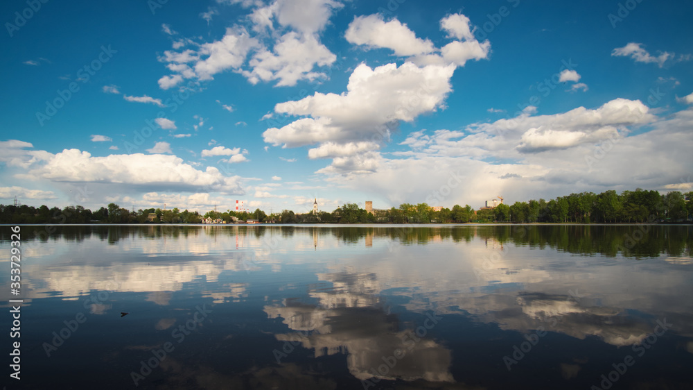 The calm idyllic landscape. The reflection of the blue sky and white clouds in a lake water