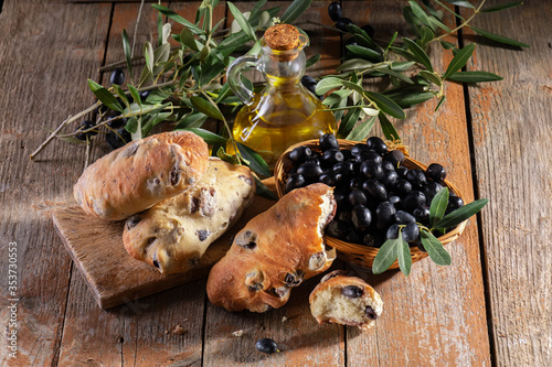 Traditional italian puccia breads with black olives on a cutten board with olive oil and olive brach and fresh black olives photo