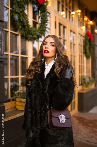 Obraz na płótnie Beautiful young caucasian woman wearing natural dark fur coat posing for a portrait near Christmas showcase. Christmas decor. Fashion. Style. Winter clothes made of natural fur. Vertical w salonie
