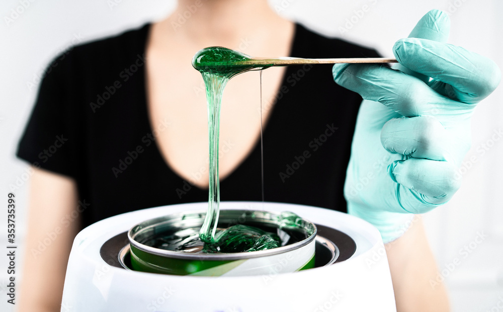 The concept of depilation and beauty is sugar paste or hair removal wax. Preparation of green wax for sugaring. Close-up sugar paste or wax honey for hair removing with wooden waxing spatula sticks.