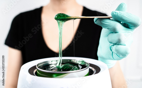 Obraz na płótnie The concept of depilation and beauty is sugar paste or hair removal wax. Preparation of green wax for sugaring. Close-up sugar paste or wax honey for hair removing with wooden waxing spatula sticks. w salonie