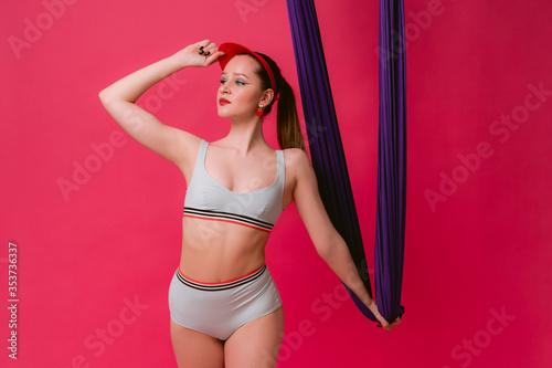 Portrait sexy attractive strong sport young womant trainer in retro swimsuit standing graceful posture put hand on cap hold on air silk looking aside with smile isolated over pink red background