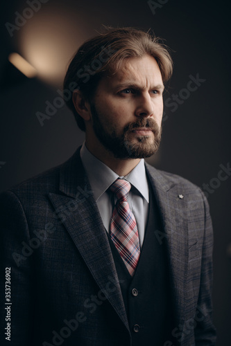 Portrait of serious bearded man in business suit standing at own office with blur background. Concept of business, finance and people.