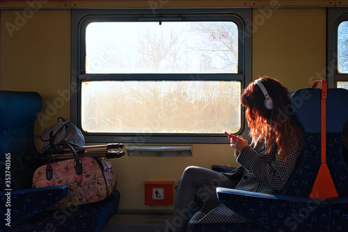 Partial view of an old second-class passenger train wagon, with a sitting young long-haired woman who watches her phone