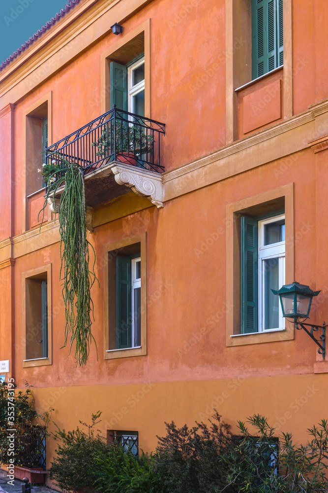 Orange stucco building with deep green and white casement windows in Athens Greece with wrought iron balcony and succulent growing down almost to ground - Close-up