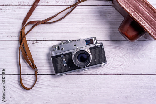 Vintage rangefinder film camera with leather case on white wooden table. The view from thetop. Old technology