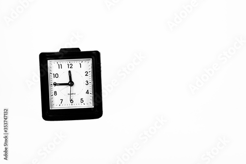 The importance of time is represented by an isolated square black framed traditional alarm clock in black and white.