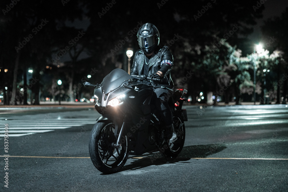 Piloto de moto con su moto detenido en la noche en la calle en la ciudad.