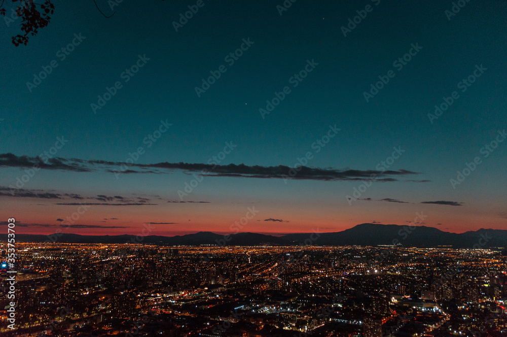 Ciudad de noche con luces encendidas entre montañas en el horizonte