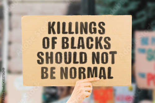 The phrase " Killings of blacks should not be normal " on a banner in men's hand with blurred background. Racism harms black people most. Stop murdered by police. Skin color harassment