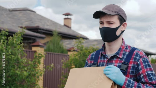 A man wearing a mask and gloves carries bags of groceries to the customer's house photo