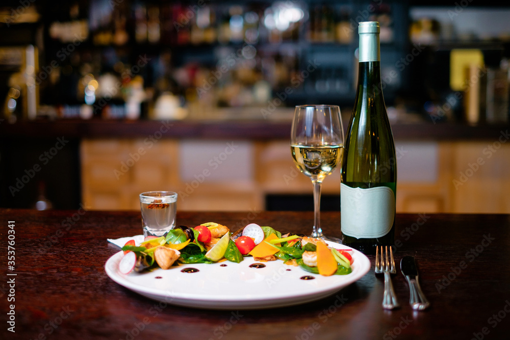 Mussel salad on a white plate with glass and bottle of wine on the background of the bar. Concept of a beautiful dish serving for a restaurant.