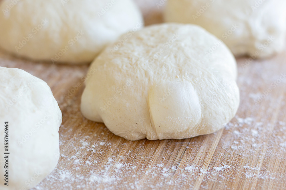 A round pieces of homemade white dough for pizza, bread or baking goods on a wooden cutting board. Small pieces of dough ready to be baked. Healthy natural family food. Side view, daylight, home 