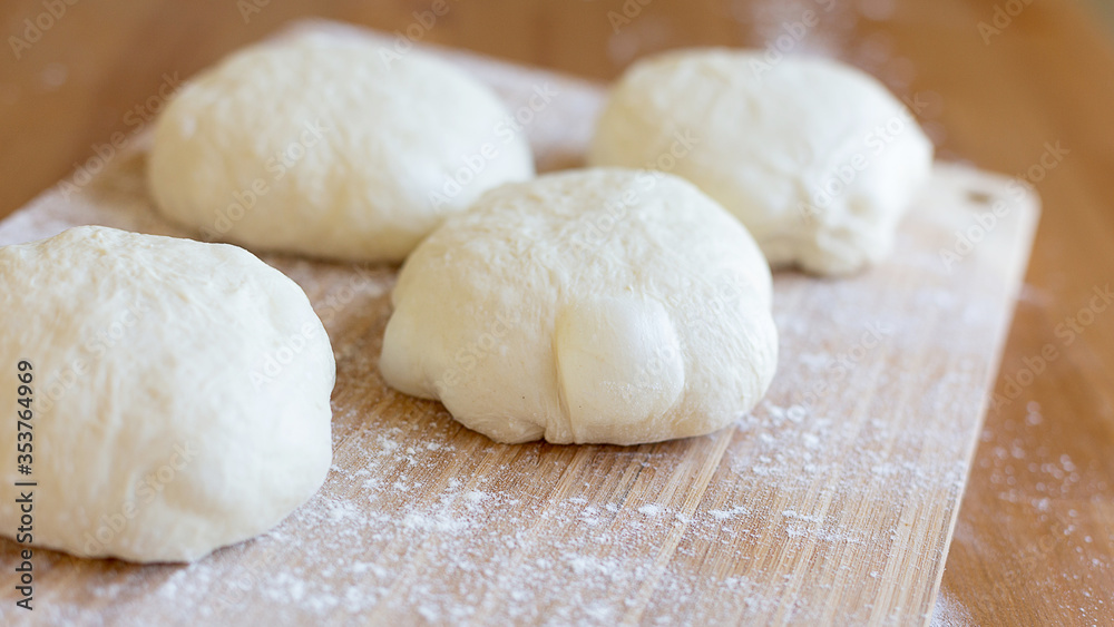 A round pieces of homemade white dough for pizza, bread or baking goods on a wooden cutting board. Small pieces of dough ready to be baked. Healthy natural family food. Side view, daylight, home 