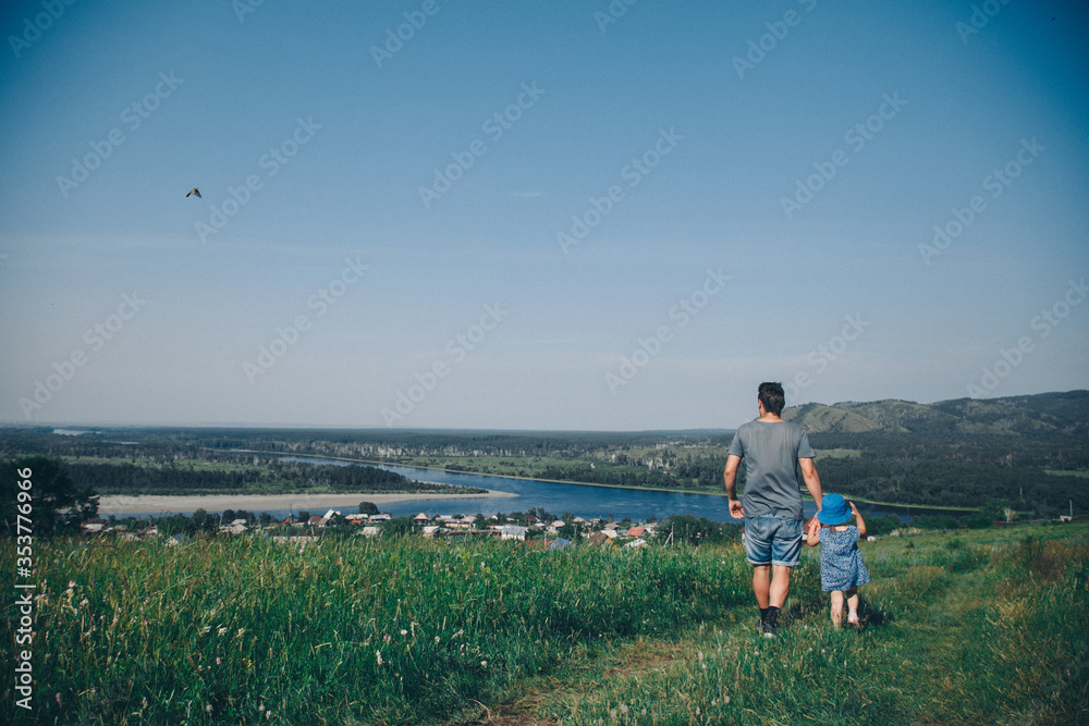 father walks with his daughter in meadow. man throws child. Village