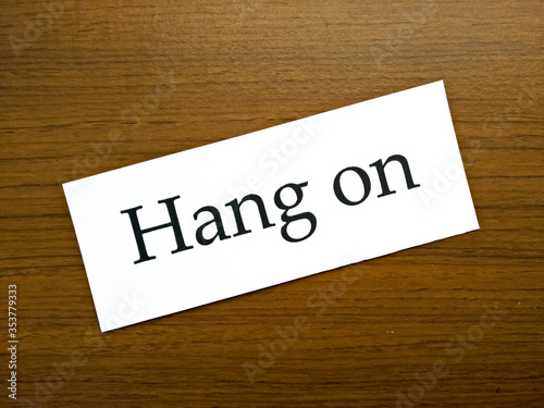 The sentence "Hang on" in white paper on wooden pattern background.