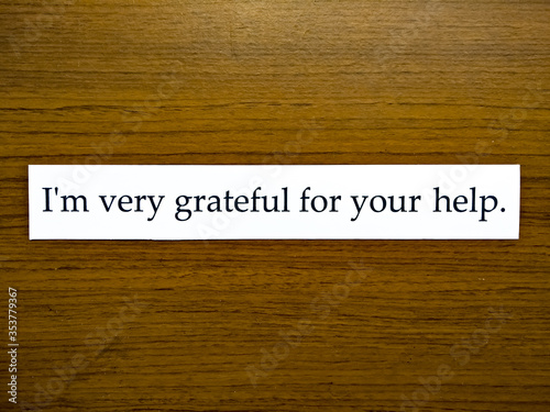The sentence "I'm very grateful for your help." in white paper on wooden pattern background.