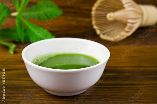 Matcha tea in a cup and green leaves with bamboo matcha tea whisk also know as chasen on a wooden background.