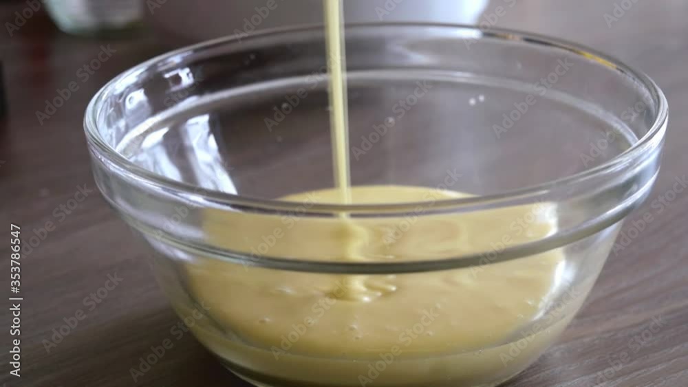 Cake batter pour into the bowl. Close view of cake batter pouring into the glass bowl