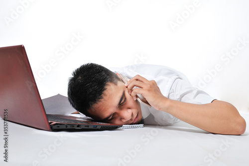 Overworked freelancer Young Asian Man Sleeping By Laptop And Phone on his ears at work tired and overloaded