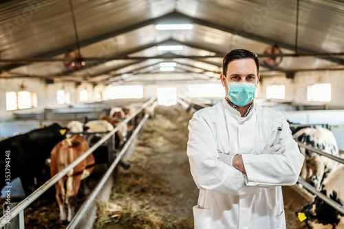 Young successful caucasian vet standing in barn with arms crossed and looking at camera.