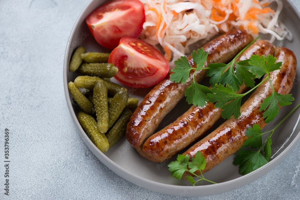 Closeup of roasted sausages with sauerkraut, gherkins, tomatoes and parsley, selective focus, studio shot