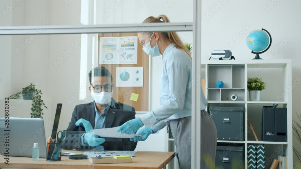 Slow motion of business people wearing face masks and gloves working in office cooperating during covid-19 global epidemic. Man is using modern laptop typing.