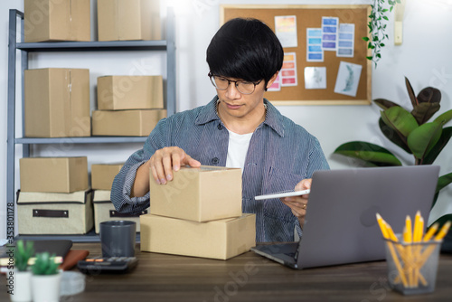 Asian man entrepreneur startup small business entrepreneur SME freelance man working with box to online marketing packaging and delivery scene at home office, onlinebusiness seller concept. photo