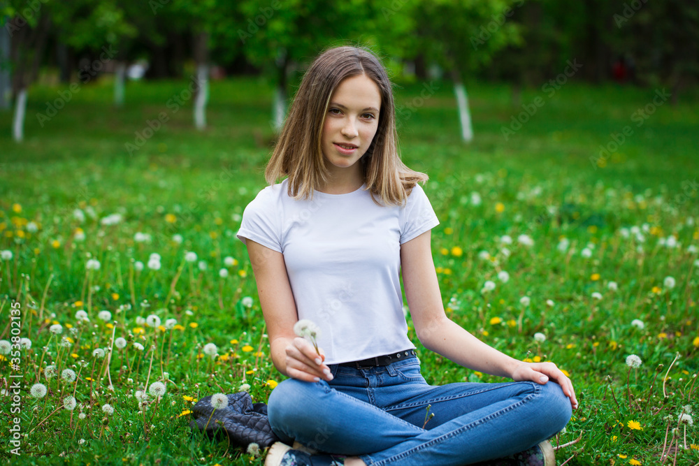 Portrait of a young beautiful girl sitting in a dandelion field a dandelion
