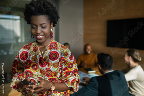 Smiling African businesswoman texting after a boardroom meeting