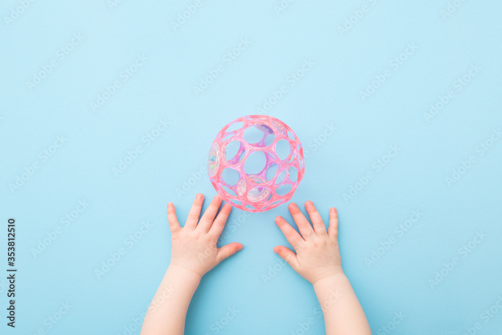 Baby hands and pink plastic ball with holes on light blue table background. Pastel color. Closeup. Toys of development for little kids. Point of view shot. Top down view. Baby hands and pink plastic ball with holes on light blue table background. Pastel color. Closeup. Toys of development for little kids. Point of view shot. Top down view.