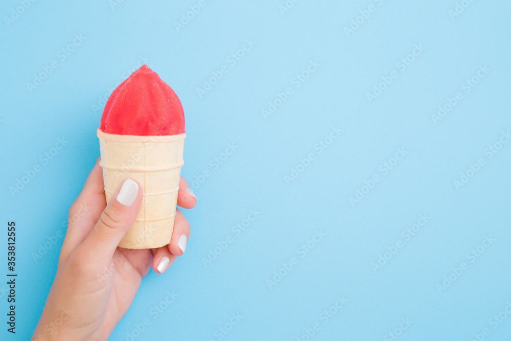Young woman hand holding ice cream with pink glaze in waffle cup on light blue background. Pastel color. Empty place for text. Closeup. Fron view. Young woman hand holding ice cream with pink glaze in waffle cup on light blue background. Pastel color. Empty place for text. Closeup. Fron view.